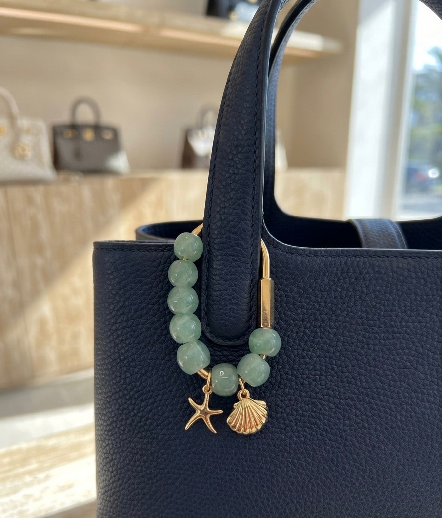 Hand-beaded bag charm with jade beads and gold starfish and shell charms clipped to a leather tote handle