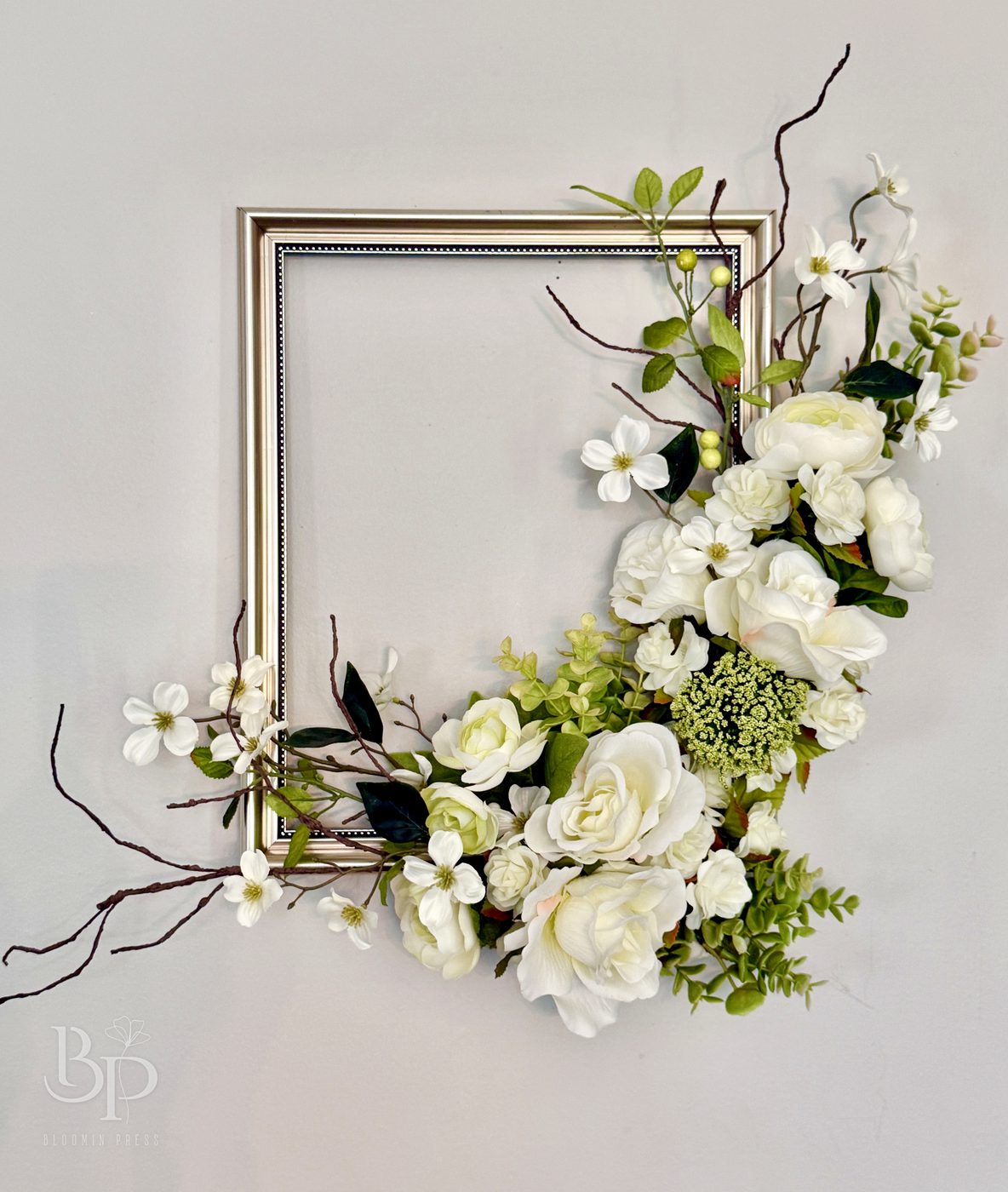 White roses, blossoms and greenery spilling across the corner of a vintage open picture frame