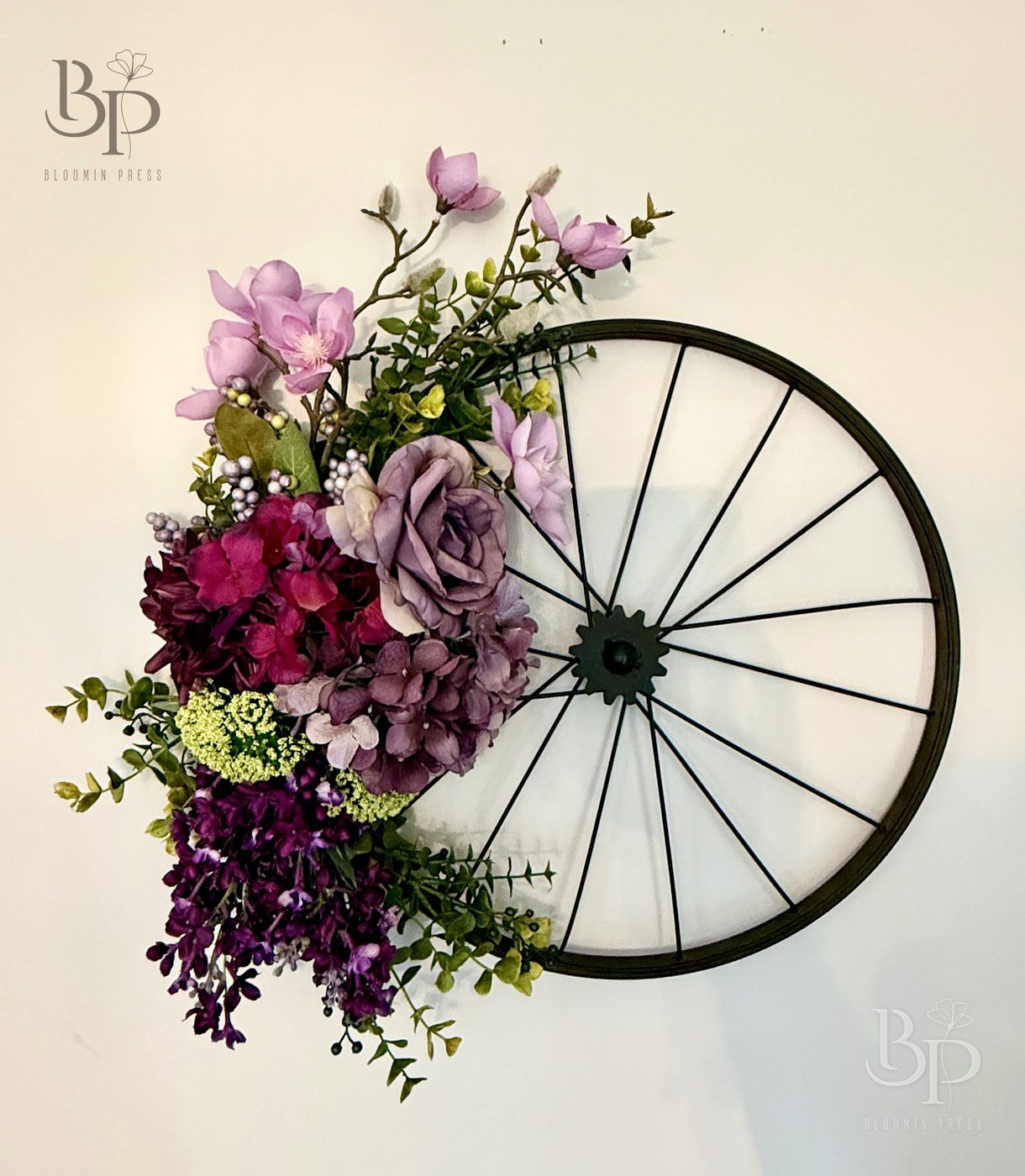 Plum and lavender flowers wrapped around a black wagon wheel