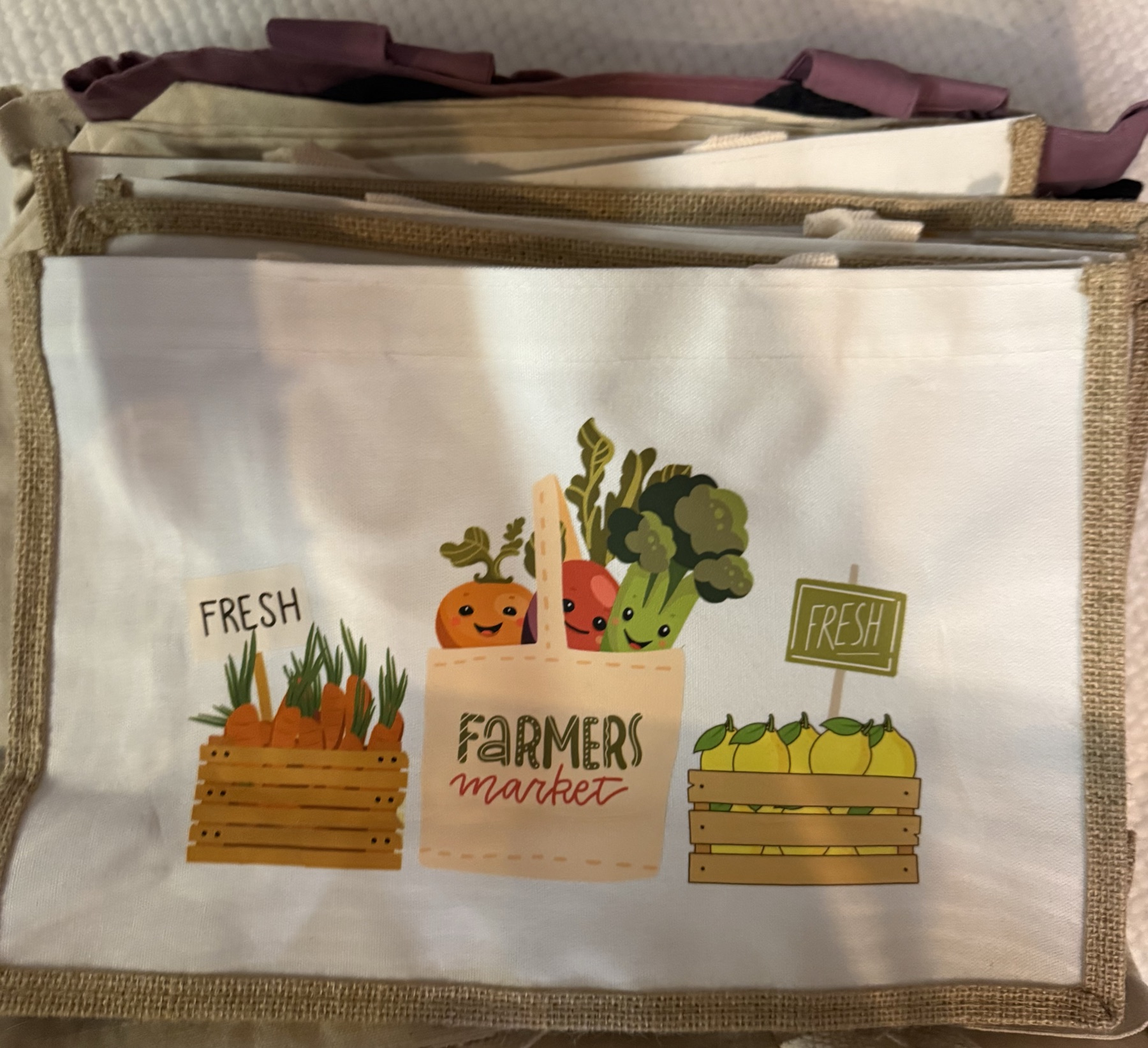 Canvas tote bag with a jute trim, printed with a farmers market design of vegetable crates and a produce basket